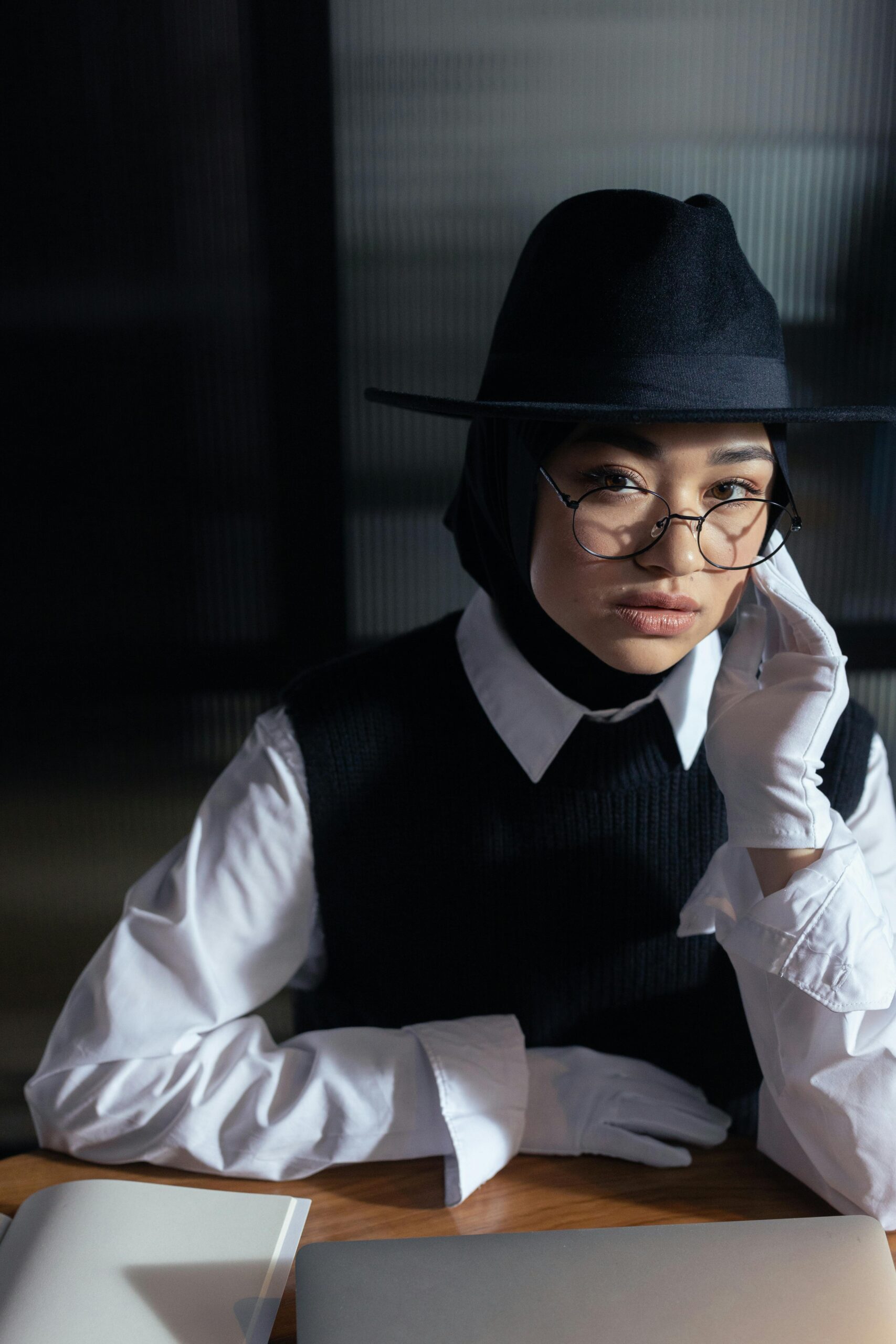 Home Stylish woman wearing glasses and hat, posing indoors with elegant attire.