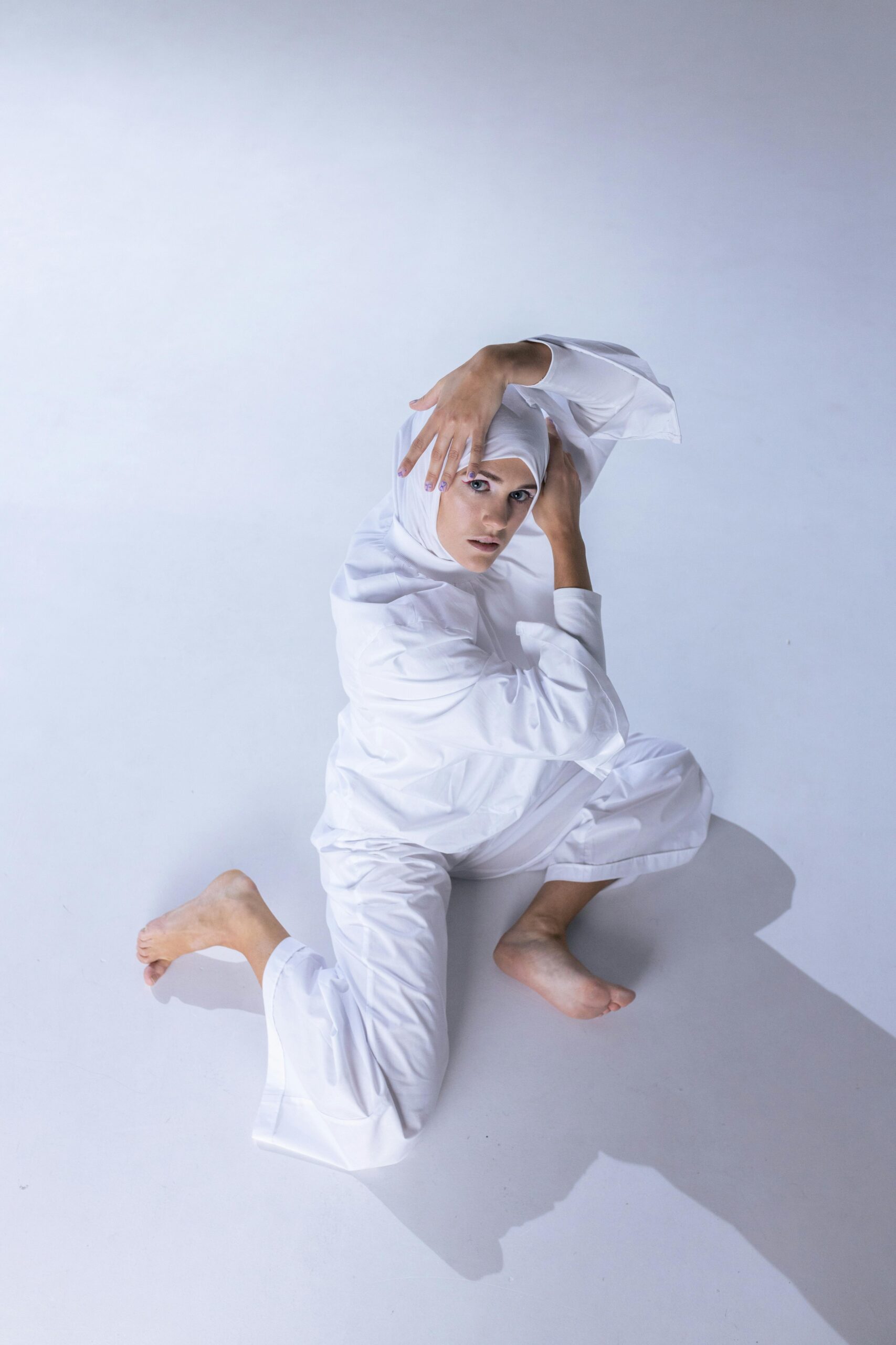 Home Muslim woman in a white outfit striking a contemporary dance pose indoors on a white background.