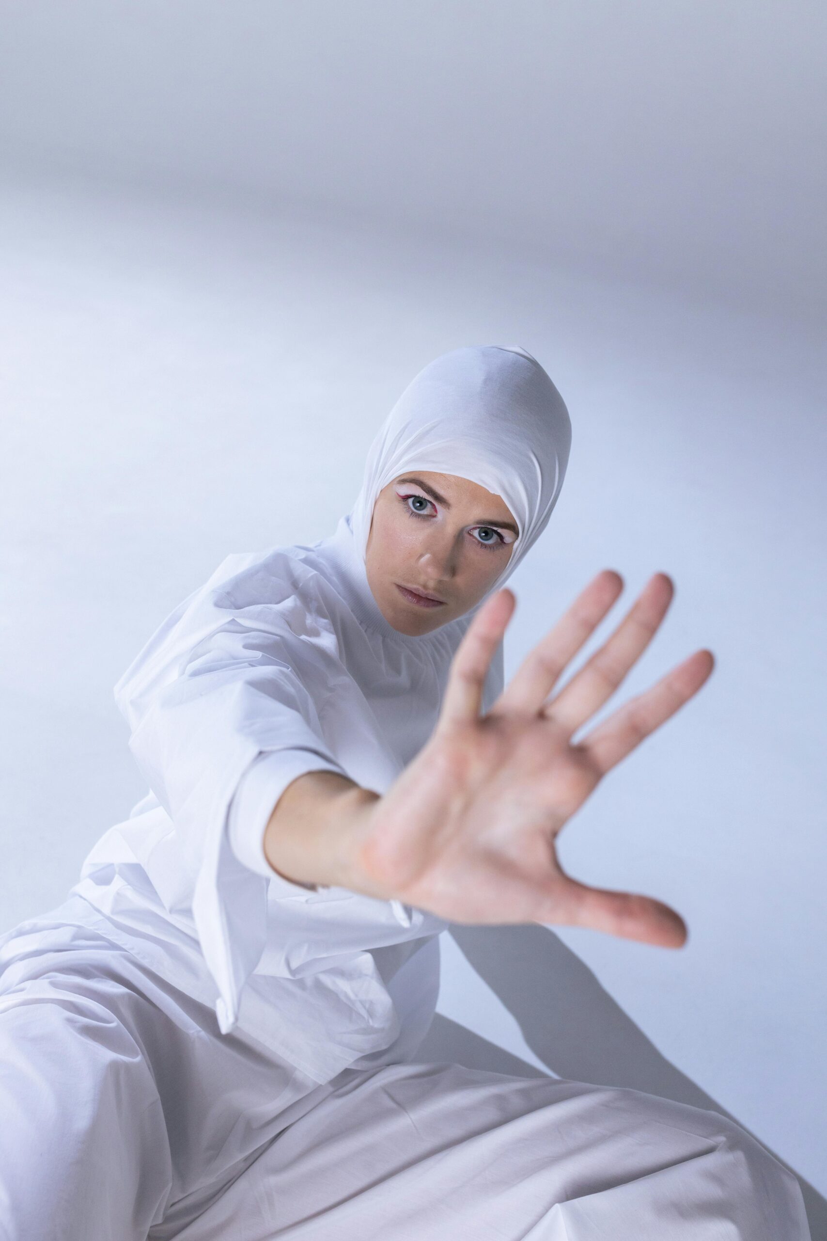 Home Dramatic portrait of a woman in a white headscarf reaching out against a white background.