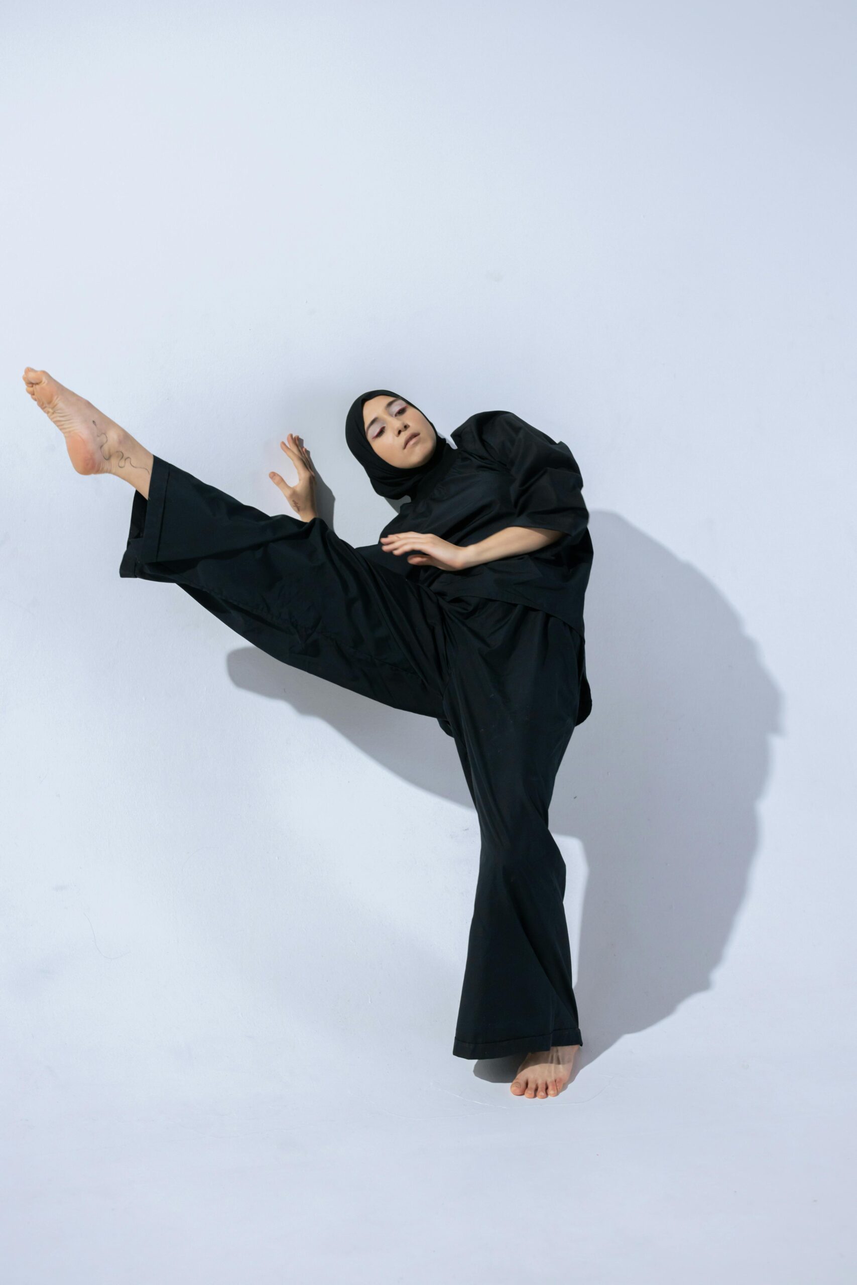 Home A Muslim woman in a hijab performing an expressive dance move in a studio setting.
