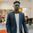 A student stands confidently in a college library surrounded by peers working on laptops.